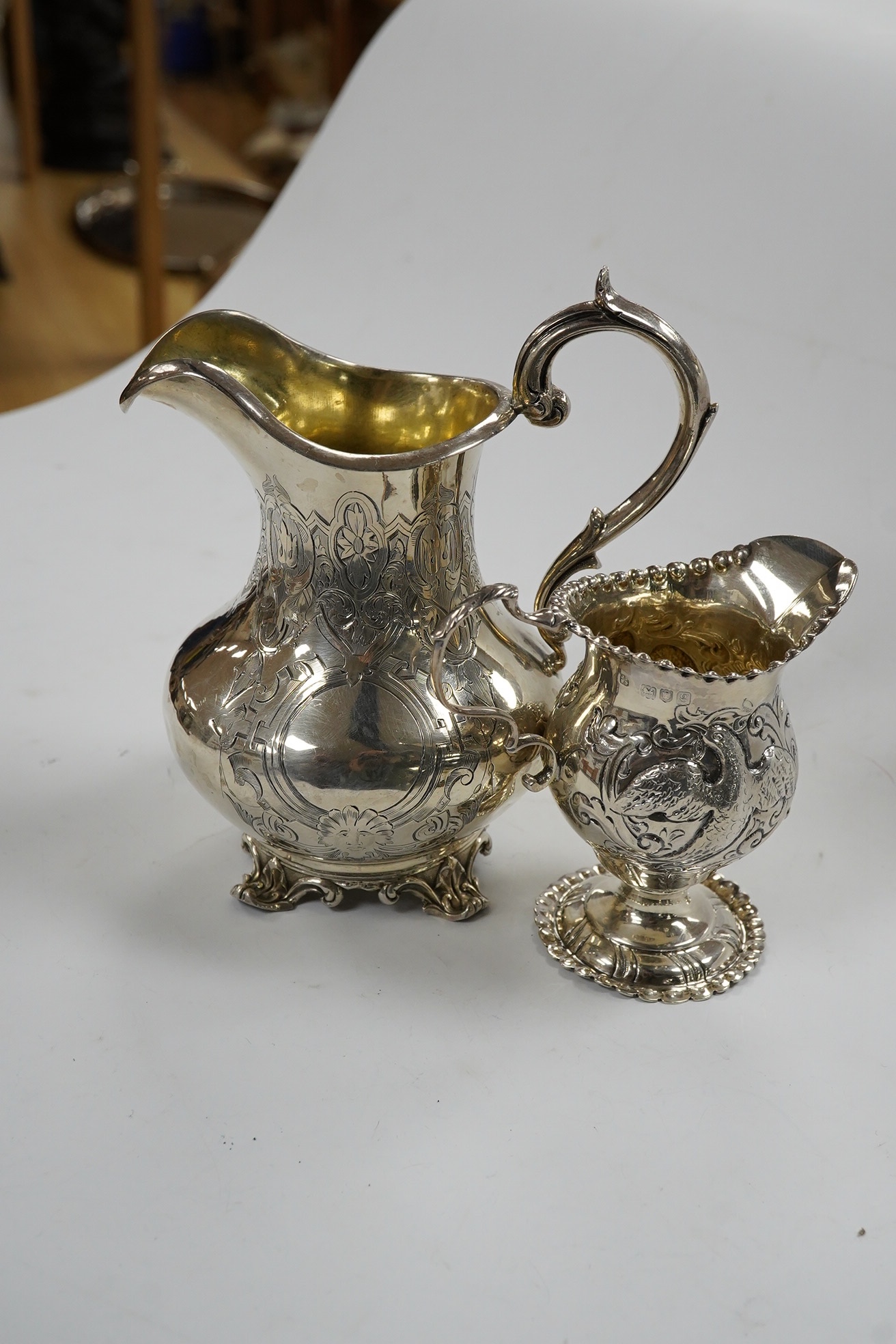 A Victorian engraved silver baluster cream jug, Henry Holland, London, 1862, 15cm, together with an Edwardian embossed silver cream jug, London, 1902, 10.5oz. Condition - poor